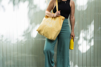 Anonymous satisfied female standing with eco friendly shopping bag in street in summer and looking away