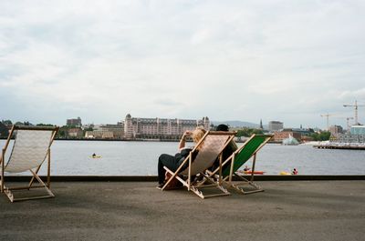 Deck chairs by sea against sky in city