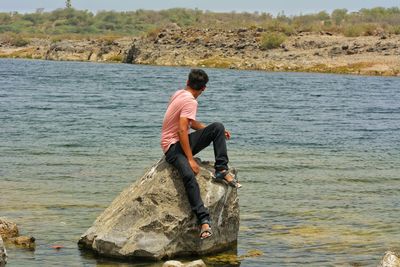 Man sitting on rock in sea