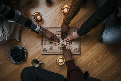 Directly above shot of multiracial friends using ouija board sitting on hardwood floor