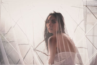 Portrait of young woman seen through white transparent curtain