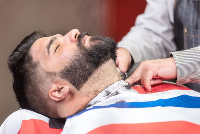 Midsection of barber shaving male customer beard in salon