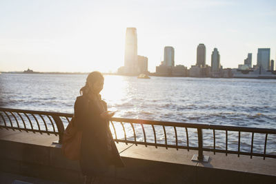 Young asian businesswoman looking at her smartphone standing on river promenade