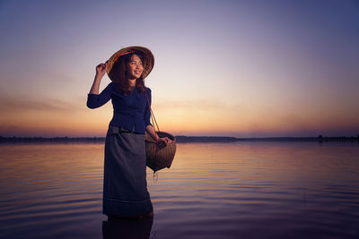 Woman standing by sea against sky during sunset