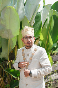 Young man wearing traditional clothing standing against plants