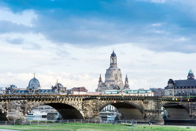 Bridge over river in city against cloudy sky