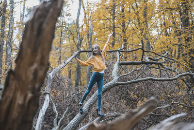 Full length of girl standing on tree trunk in forest