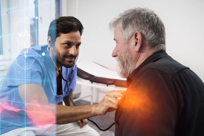 Male doctor examining senior patient with stethoscope