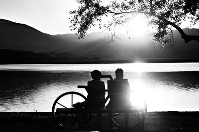 Rear view of men sitting by lake against sky