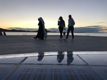 People standing by sea against sky during sunset