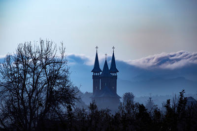 Low angle view of silhouette trees and building against sky