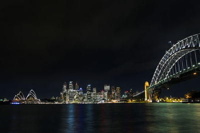 Illuminated city by sea against sky at night