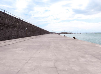 Empty footpath by sea against sky