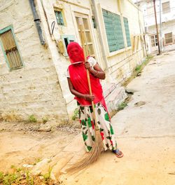 Woman holding broom while standing against building