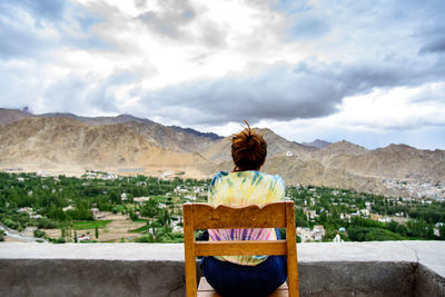 Rear view of woman sitting on chair against mountain 