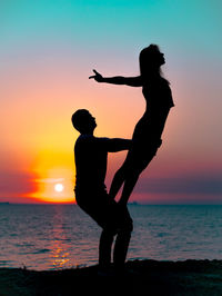 Silhouette couple exercising at beach against sky during sunset