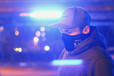 Thoughtful man wearing mask amidst illuminated lights at night