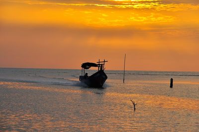 Silhouette man in boat sailing in sea against sky during sunset