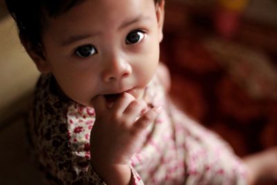 Portrait of cute girl biting finger while sitting at home