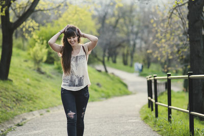 Smiling woman standing on footpath by railing at park