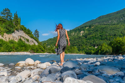 Woman standing on rock by mountain against sky