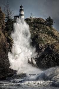 Sea waves splashing on rock against sky