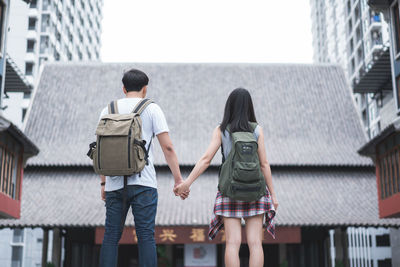 Rear view of friends walking on building in city