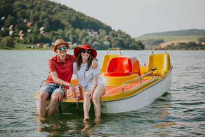 Cheerful man and woman in paddleboat on lake against sky