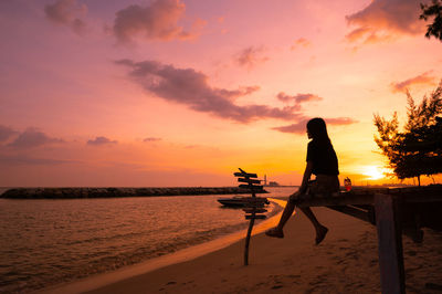 Silhouette woman standing on beach against sky during sunset