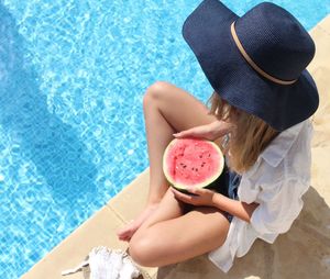 High angle view of woman holding watermelon while sitting at poolside