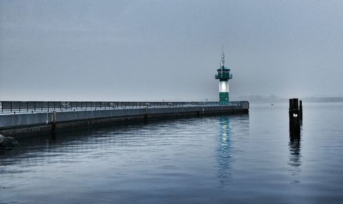 Lighthouse on pier in sea against sky