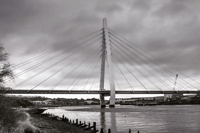 Suspension bridge over river against cloudy sky