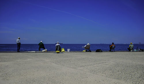 People on beach against clear blue sky