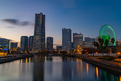 Illuminated buildings by river against sky in city