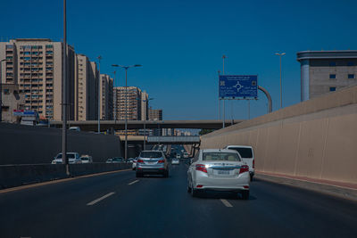 Cars on road by buildings against blue sky