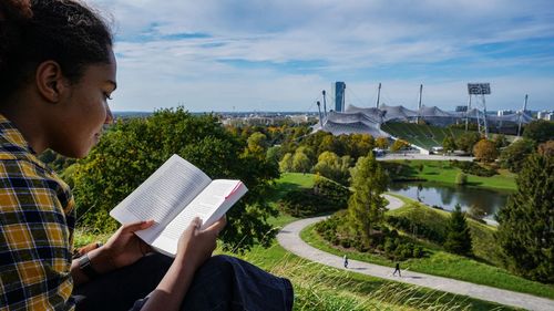 Pretty young woman is reading a book while sitting on the olympiaparkhill 