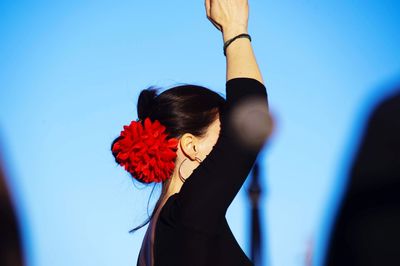 Portrait of woman with pink flowers against blue sky