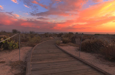 Boardwalk against cloudy sky during sunset