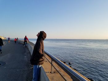 Rear view of woman walking on shore against clear sky