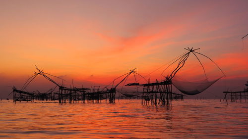 Silhouette fishing net in sea against orange sky