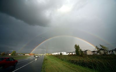 Rainbow over road against cloudy sky