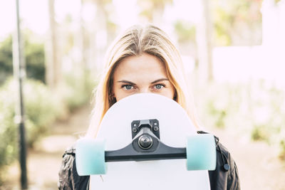 Portrait of young woman with skateboard in park