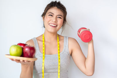 Portrait of smiling woman holding apple against white background