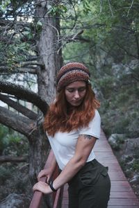 Young woman standing by railing against trees in forest