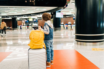 Child boy with backpack  in the airport terminal, waiting for flight, travel with suitcase. vacation