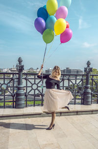 Woman with colorful balloons on walkway against sky in city