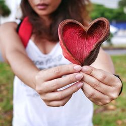 Midsection of woman holding heart shape flower while standing outdoors