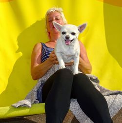 Portrait of woman with dog sitting against yellow wall