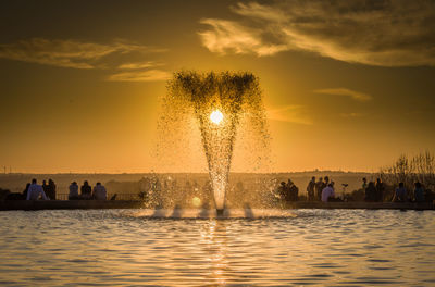 Silhouette people at illuminated fountain against sky during sunset