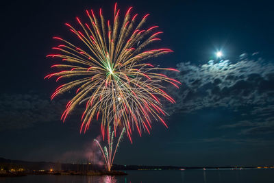 Firework display over sea against sky at night